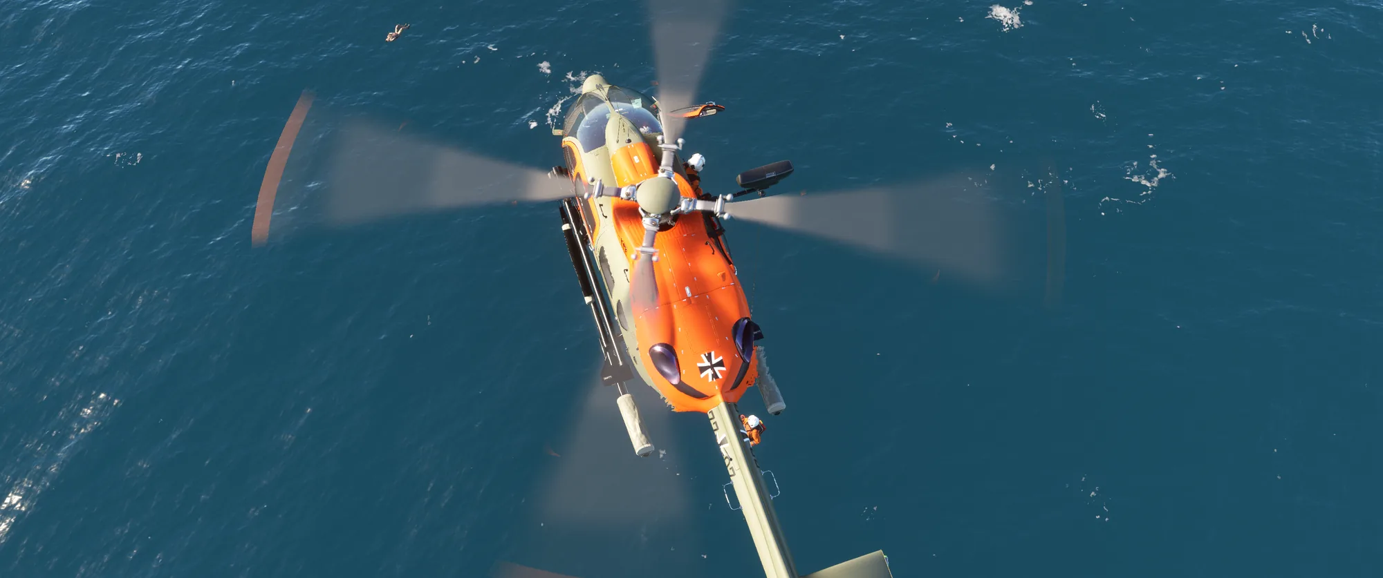 Orangefarbener Such- und Rettungshubschrauber von oben über dem Meer, an der Winde hängt ein Retter